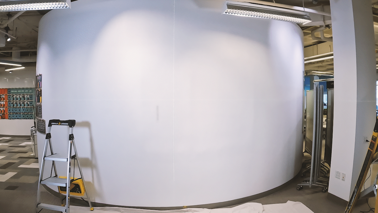 two men install the mural decal on the wall with a ladder